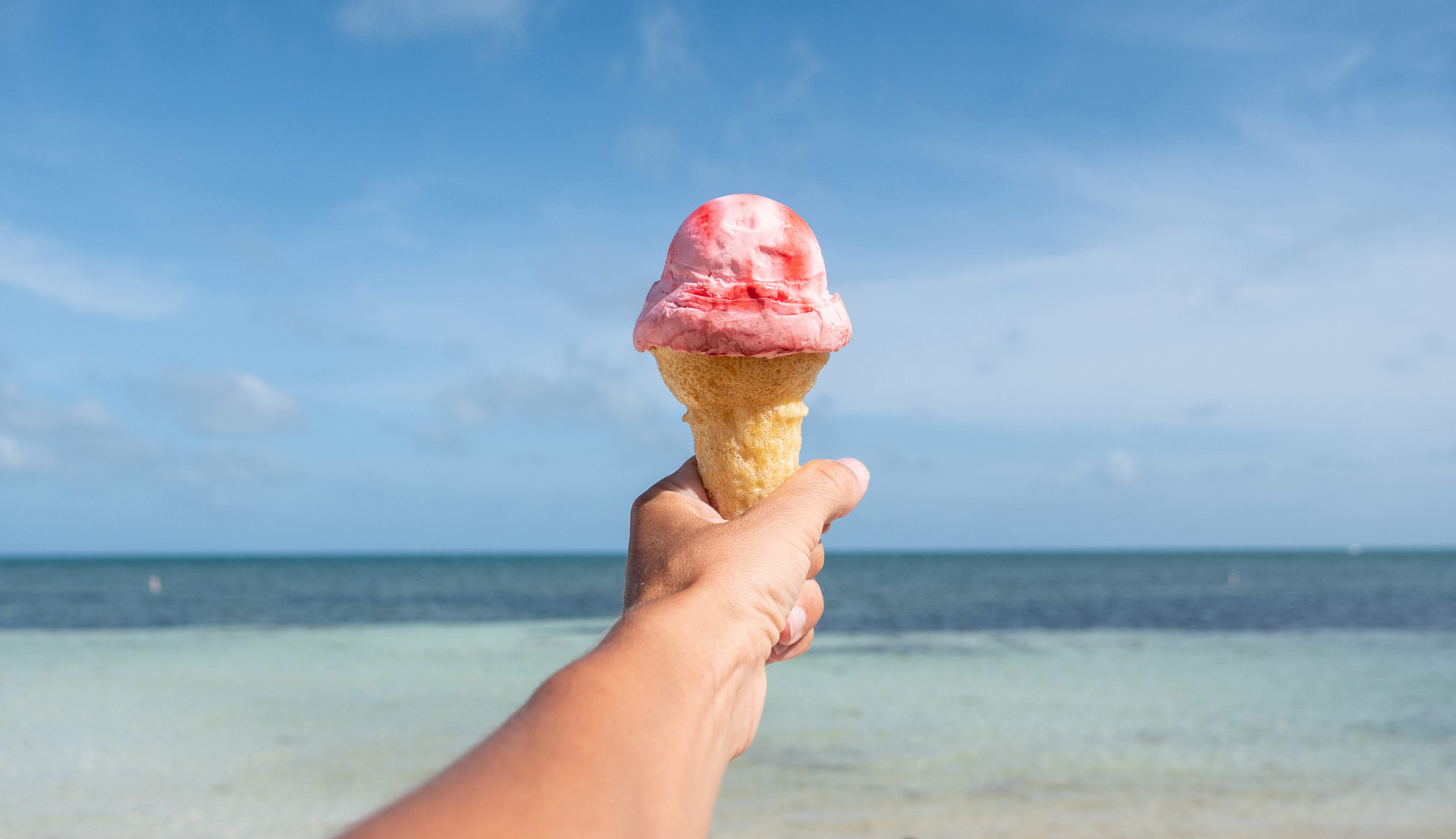 Photo of person holding up ice cream looking out at crystal blue waters